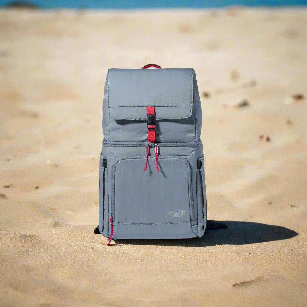 A Coleman 18-Can Soft-Sided Backpack Cooler in gray and red, featuring Temp-Lockâ„¢ insulation and a leakproof liner. The eco-friendly design includes padded straps, expandable side pockets for water bottles, and a front zipper pocket for valuables. Perfect for keeping drinks and snacks cool on outdoor adventures like picnics, camping, and beach trips.