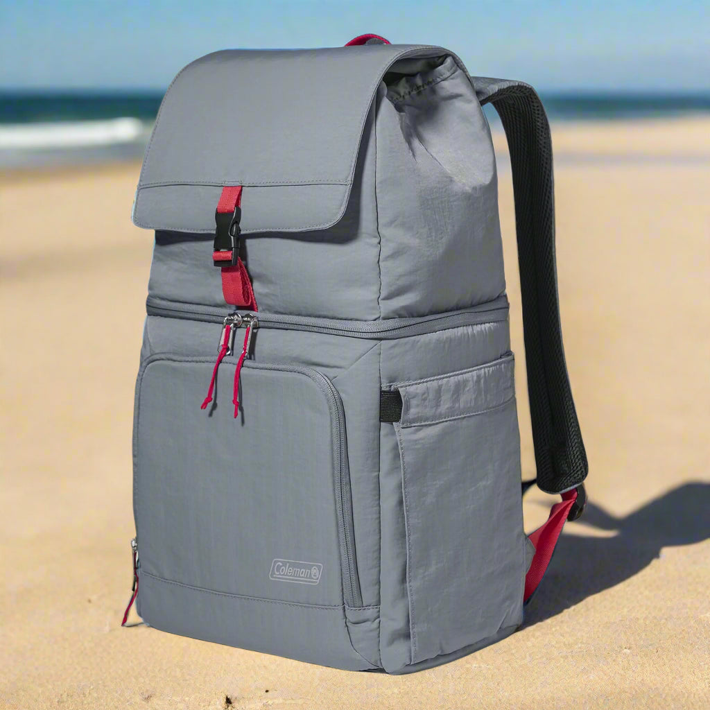 A Coleman 18-Can Soft-Sided Backpack Cooler in gray and red, featuring Temp-Lockâ„¢ insulation and a leakproof liner. The eco-friendly design includes padded straps, expandable side pockets for water bottles, and a front zipper pocket for valuables. Perfect for keeping drinks and snacks cool on outdoor adventures like picnics, camping, and beach trips.
